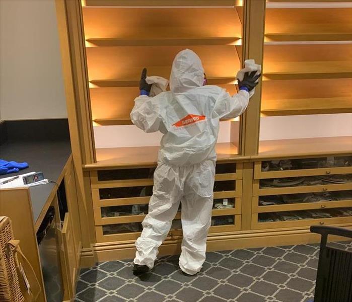 Employee cleaning shelves while wearing hazmat suit. 